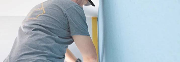 Person klebt Malerband an Wand